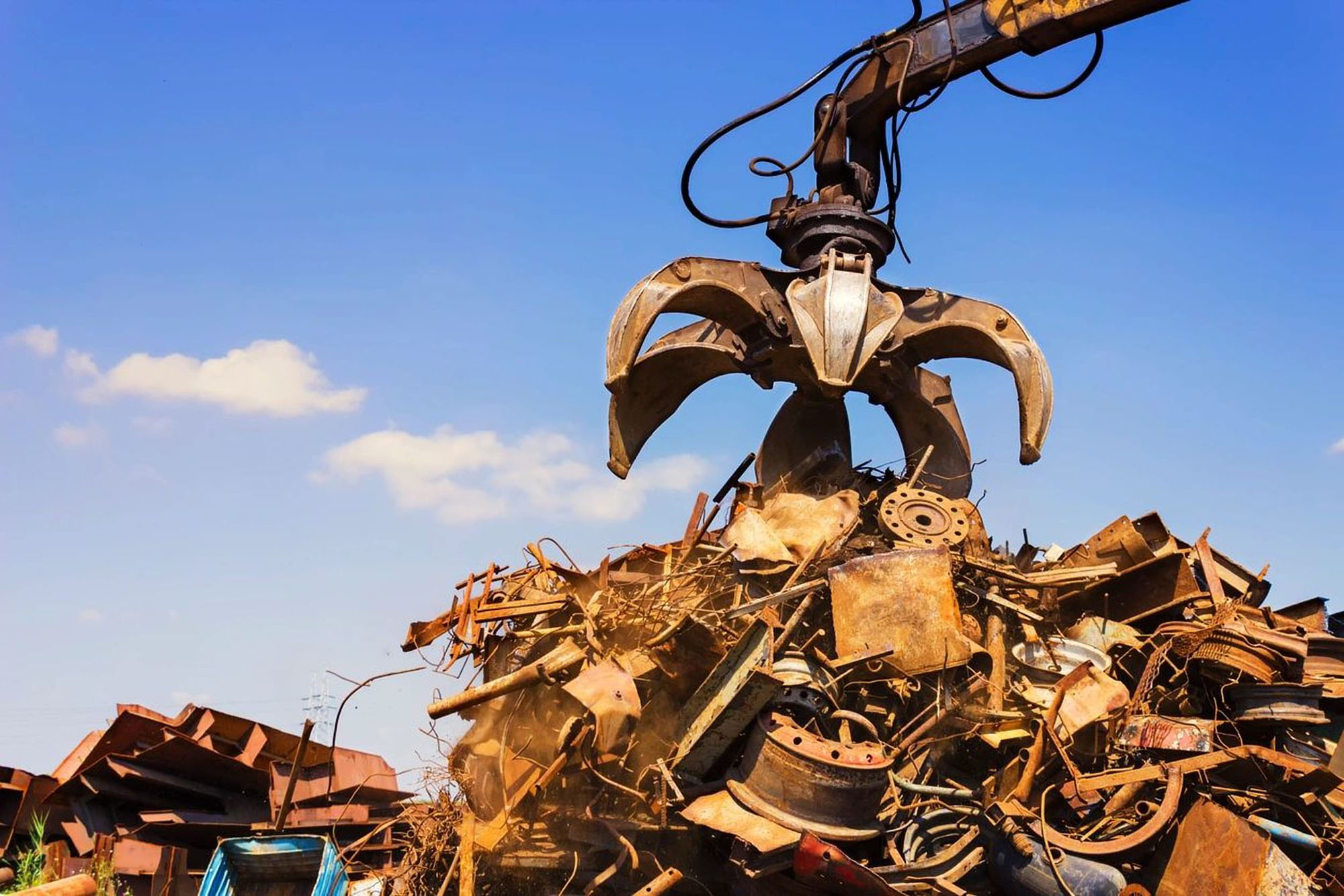 Mechanical claw lifting scrap metal at a recycling yard.